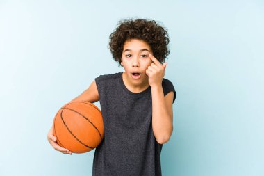 Mavi arka planda izole edilmiş basketbol oynayan çocuk işaret parmağıyla bir hayal kırıklığı gösteriyor..