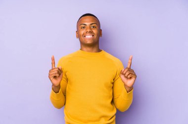 Mor arka planda izole edilmiş genç latin adam iki ön parmağı da boş bir alan gösteriyor..