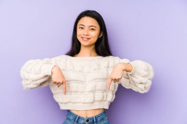 Mor arka planda izole edilmiş genç Çinli kadın parmaklarıyla aşağıya bakıyor, olumlu bir his..