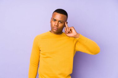 Mor arka planda izole edilmiş genç Latin bir adam şakağı parmağıyla işaret ediyor, düşünüyor ve bir göreve odaklanıyor..