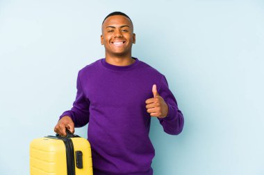 Genç gezgin bir bavul tutuyor, izole edilmiş gülümsüyor ve başparmağını kaldırıyor.