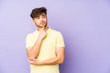 Mor arka planda izole edilmiş genç bir Arap şüpheli ve şüpheci bir ifadeyle yana bakıyor..