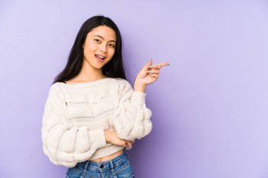 Mor arka planda izole edilmiş genç Çinli kadın işaret parmağıyla işaret ederek gülümsüyor..