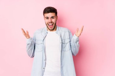 Beyaz arka planda poz veren beyaz tenli genç bir iş adamı zaferi ya da başarıyı tek başına kutluyor, şaşırıyor ve şok oluyor..