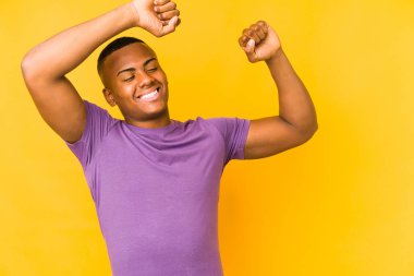 Sarı arka planda izole edilmiş genç latin adam. Kollarını uzatıyor, rahat duruyor..