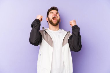 Mor arka planda izole edilmiş genç beyaz adam zafer kazandıktan sonra yumruğunu kaldırıyor, kazanan konsept..