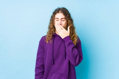 Uzun saçlı adam tek başına esniyor. Ağzı eliyle kapatan yorgun bir hareket sergiliyor..