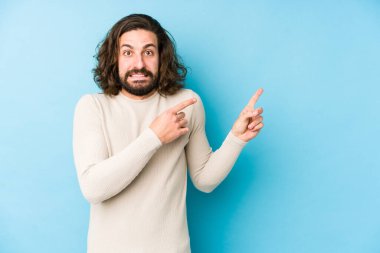 Mavi arka planda izole edilmiş uzun saçlı genç adam işaret parmağıyla fotokopi alanını işaret ederek şok oldu..