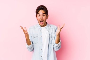 Pembe arka planda poz veren beyaz bir genç zaferi ya da başarıyı kutluyor, şaşırıyor ve şoka uğruyor..