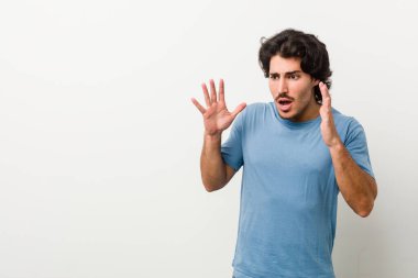 Beyaz arka planda genç yakışıklı bir adam yüksek sesle bağırıyor, gözleri açık ve elleri gergin tutuyor..