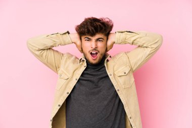 Arka planda poz veren genç bir Arap adam kulaklarını elleriyle kapatıyor ve çok fazla ses duymamaya çalışıyor..