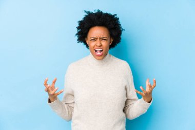 Orta yaşlı Afrikalı Amerikalı kadın mavi bir arka plana karşı öfkeyle bağırıyor..