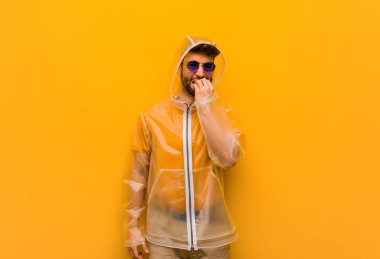 Yağmurluk giyen genç adam tırnak yiyor, gergin ve çok endişeli.