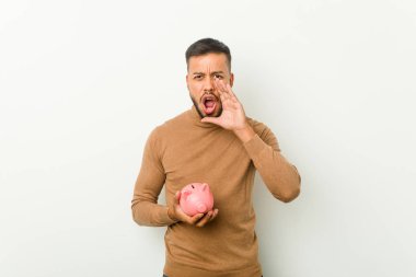 Genç Güney Asyalı adam elinde kumbarayla heyecanlı bir şekilde bağırıyor.