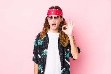 Beyaz tenli genç bir adam göz kırpıyor ve elinde iyi bir jest tutuyor..