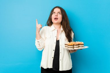 Genç, kıvrımlı bir kadın elinde kapkekleri açık ağızla yukarı doğrultuyor..