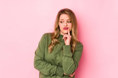 Pembe arka planda soyutlanmış beyaz bir kadın şüpheli ve şüpheci bir ifadeyle yana bakıyor..