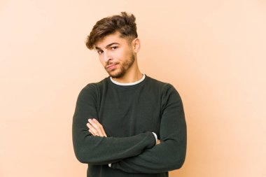 Bej arka planda izole edilmiş, hoşnutsuzca kaşlarını çatmış, kollarını kavuşturmuş genç bir Arap..