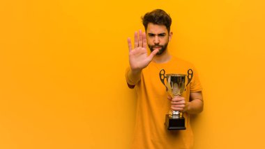 Elinde kupa tutan genç adam elini öne koyuyor.