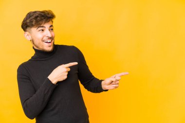 Sarı arka planda izole edilmiş genç bir Arap işaret parmaklarıyla işaret ederek heyecanlanıyor..