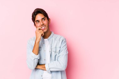Pembe arka planda poz veren beyaz genç bir adam izole edilmiş bir şekilde rahat bir şekilde fotokopi odasına bakan bir şeyi düşünüyor..