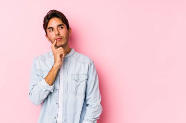Pembe arka planda poz veren beyaz bir genç şüpheli ve şüpheci bir ifadeyle yanlamasına bakıyor..