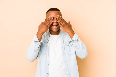 Bej arka planda izole edilmiş genç latin adam elleriyle gözlerini kapatıyor, büyük bir gülümsemeyle bir sürpriz bekliyor..