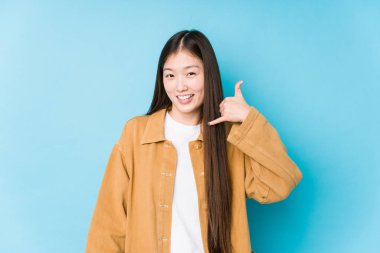 Mavi arka planda poz veren genç Çinli kadın parmaklarıyla bir cep telefonu hareketi gösteriyor..