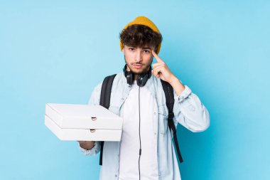 Elinde pizza tutan genç Arap öğrenci parmağıyla tapınağı işaret ediyor, düşünüyor ve bir göreve odaklanıyor..