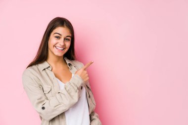 Pembe arka planda poz veren beyaz bir kadın gülümsüyor ve boş alanda bir şeyler gösteriyor..