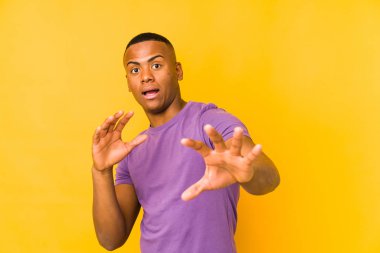 Sarı arka planda izole edilmiş genç latin adam yakın bir tehlike nedeniyle şoka uğruyor.