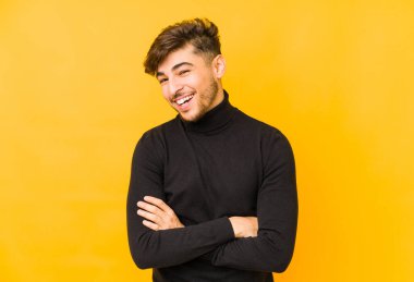 Sarı arka planda yaşayan genç bir Arap adam gülüyor ve eğleniyor..