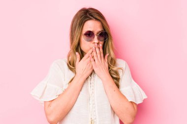 Pembe arka planda gözlüklü, ağzı kapalı, elleri endişeli görünen beyaz bir kadın..