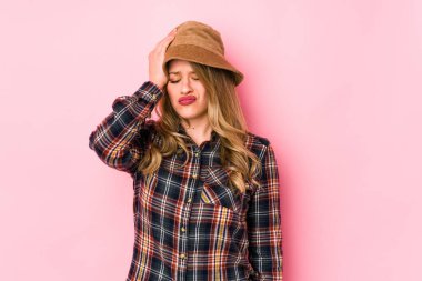 Şapka takan genç, beyaz bir kadın yorgun ve uykulu bir şekilde elini başının üstünde tutuyor..