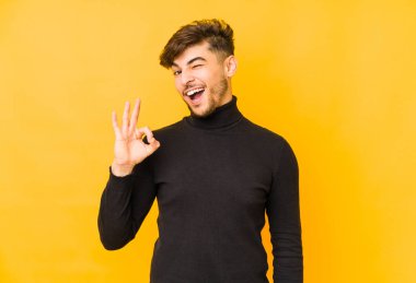 Sarı arka planda izole edilmiş genç bir Arap göz açıp kapayıncaya kadar iyi bir el hareketi yapar..