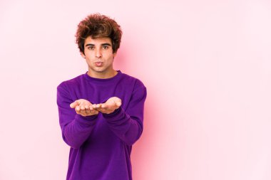 Pembe arka planda genç beyaz bir adam izole edilmiş dudaklar ve hava öpücüğü göndermek için avuç içleri tutuyor..