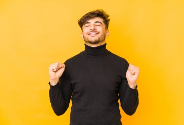 Sarı arka planda izole edilmiş genç bir Arap, mutlu ve başarılı hissediyor. Zafer konsepti.