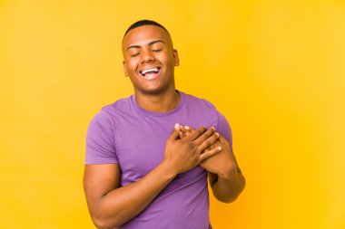 Sarı arka planda izole olmuş genç latin adam gülüyor, ellerini kalbe koyuyor, mutluluk kavramını koruyor..