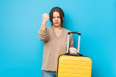 Kameraya yumruğunu gösteren bir bavul tutan kıvrımlı genç kadın, agresif yüz ifadesi..