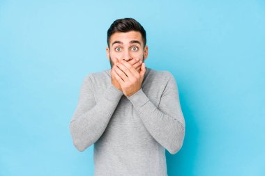 Mavi arka planda genç bir beyaz adam izole edildi. Ellerle ağzını kapatarak şok geçirdi..