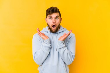 Sarı arka planda izole edilmiş genç beyaz adam şaşırdı ve şok oldu..