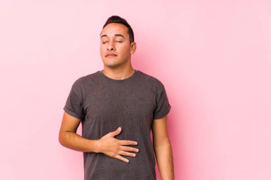 Yog Latin adam pembe arka planda poz veriyor karnına dokunuyor, nazikçe gülümsüyor, yemek yiyor ve tatmin oluyor..