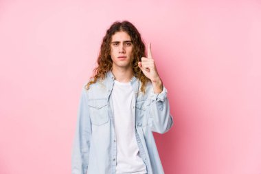 Uzun saçlı adam yalnız poz veriyor. Bir numarayı parmağıyla gösteriyor..