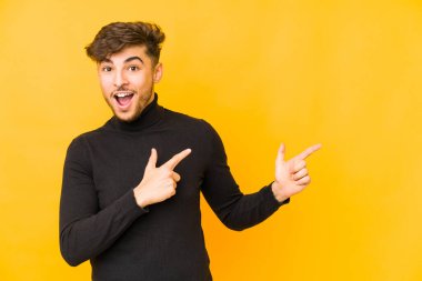 Sarı arka planda izole edilmiş genç bir Arap adam işaret parmağıyla fotokopi alanını işaret ederek heyecan ve arzuyu ifade ediyor..