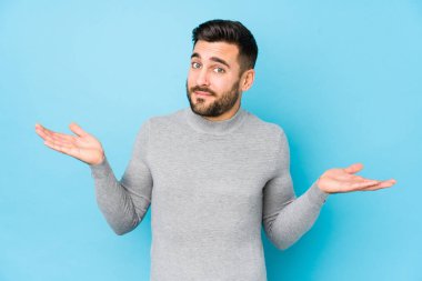 Mavi arka planda genç beyaz bir adam şüpheli ve omuz silkip sorgulama hareketi yapıyor..