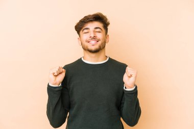 Genç Arap bir adam bej bir arka planda izole edilmiş mutlu ve başarılı hissediyor. Zafer konsepti.