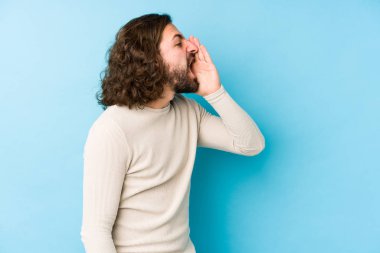 Uzun saçlı genç adam mavi bir arka planda izole edilmiş bağırıyor ve avuç içini açık tutuyor..