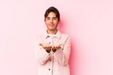 Pembe arka planda poz veren beyaz bir genç avuçlarıyla bir şey tutuyor ve kameraya sunuyor..