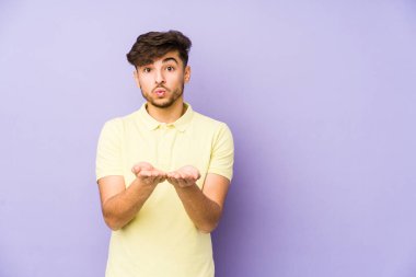 Mor bir arka planda izole edilmiş genç bir Arap. Dudakları kıvrılmış ve avuç içleri havada öpüşmek için tutulmuş..