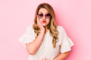 Pembe arka planda izole edilmiş gözlüklü genç beyaz kadın yanakları patlatıyor, yorgun bir ifade takınıyor. Yüz ifadesi kavramı.